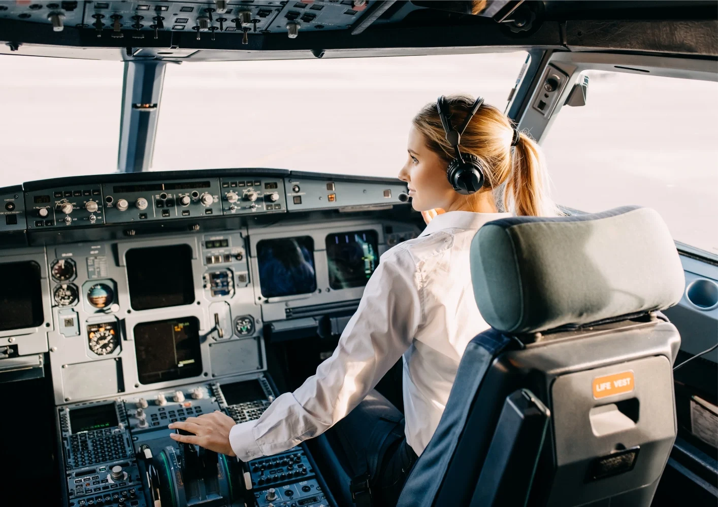 Female pilot at controls inside commercial jet cockpit wearing headset.