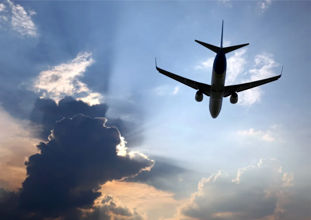 Commercial airplane climbing through dramatic clouds with sunlit sky behind.