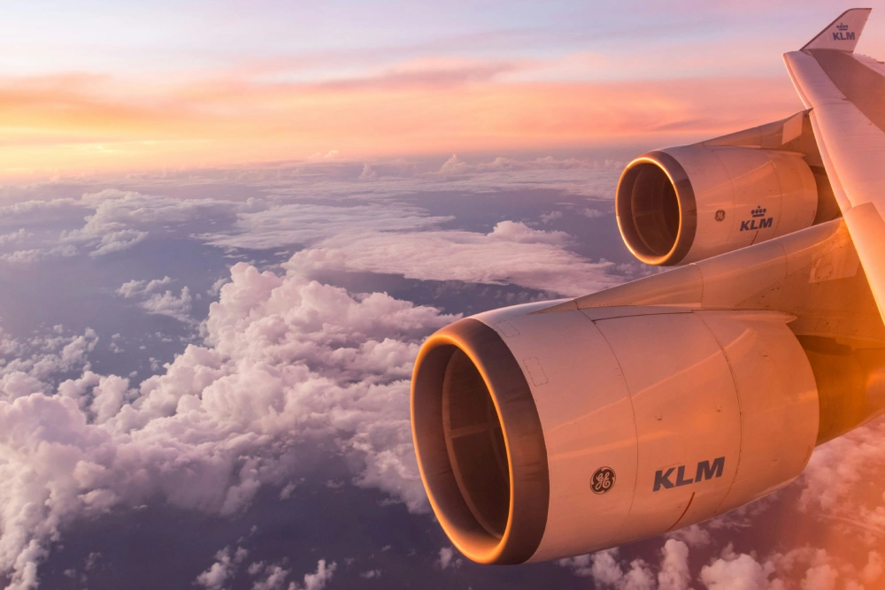 Twin KLM jet engines glowing at sunrise above expansive cotton clouds.