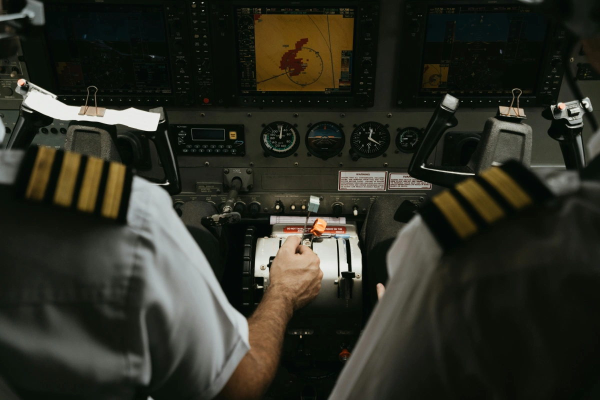 Pilots adjust throttle quadrant together in dimly lit modern cockpit.