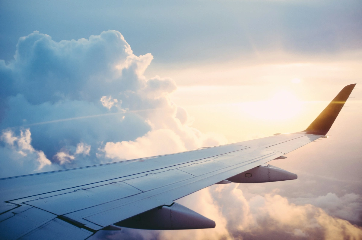 Wing extends toward sunlit clouds, cabin view amid bright morning sky.