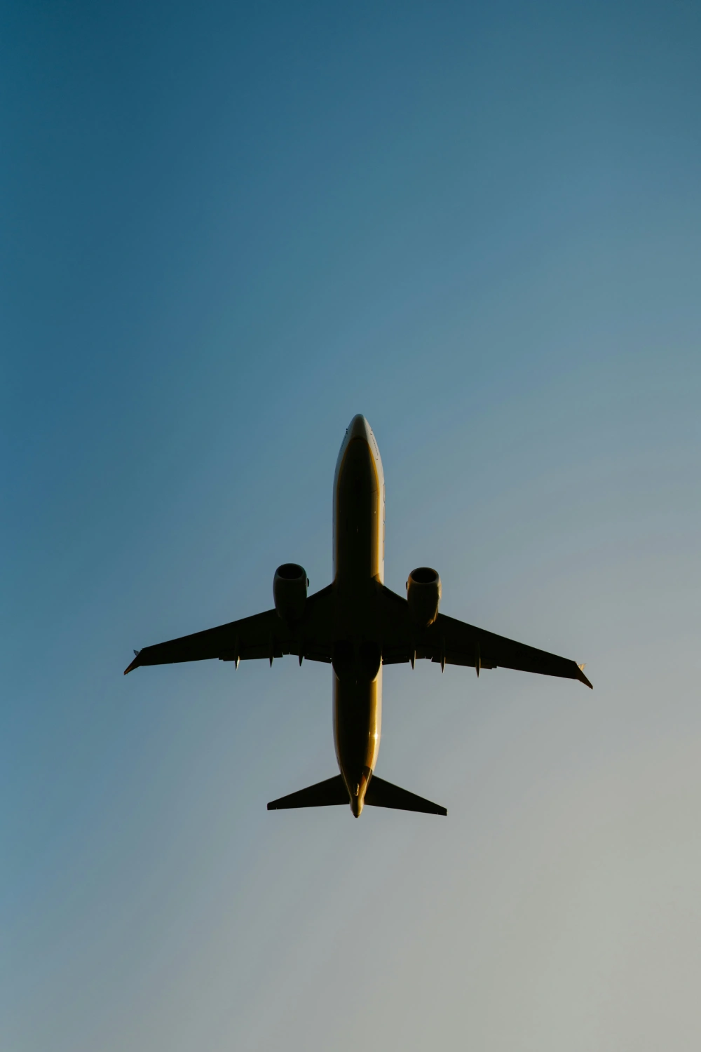 Silhouette of passenger jet seen from below against clear blue sky.